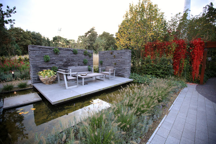 Декоративные злаки у прудика с патио Декоративные злаки у прудика с патио на фоне живой изгороди из дикого винограда